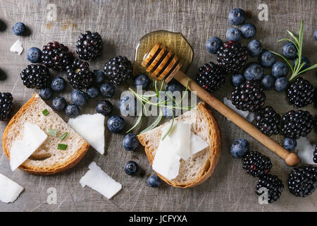 Beeren-Brombeere und Heidelbeere, Honig auf Dipper, Rosmarin, Ziegenkäse mit Brot serviert über grau Metall Textur Hintergrund geschnitten. Sommer-Sandwich. Stockfoto