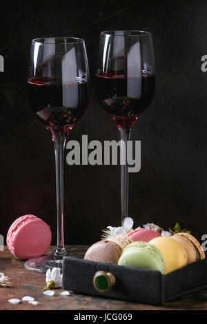 Zwei Gläser Portwein mit Vielzahl von bunten französische Süßspeise Macaron Makronen mit unterschiedlichen Füllungen serviert mit Frühlingsblumen über dunkel Stockfoto