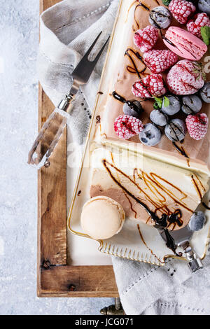 Drei Schichten Vanille, Kaffee und Schokolade Eis Kuchen, serviert mit gefrorenen Beeren und Makronen Kekse auf rechteckigen weißen Teller, Textile napki Stockfoto