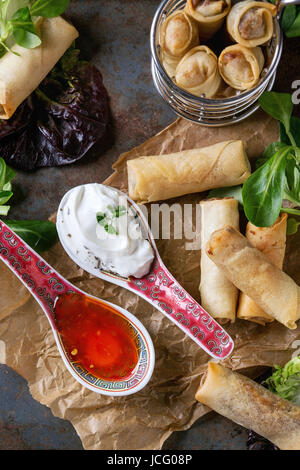 Frittierte Frühlingsrollen mit roten und weißen Saucen in China Löffel serviert auf zerknittertes Papier und Braten Korb mit grünem Salat und hölzerne Stäbchen über o Stockfoto