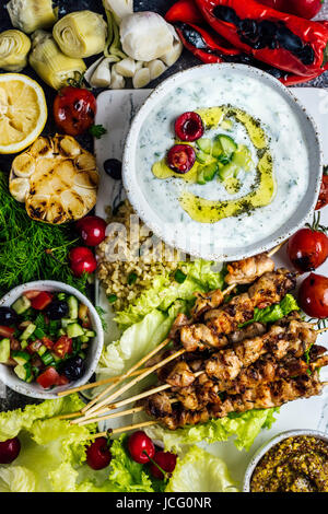 Hähnchen-Spieße auf eine weiße Tafel serviert mit einer Schüssel Cacik und eine Gurke und Joghurt-Dip und mit verschiedenen Snacks aus der Ansicht von oben fotografiert. Stockfoto