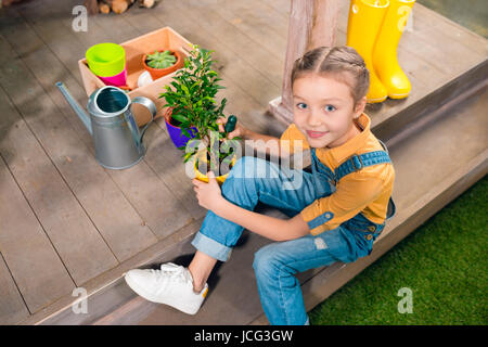 Erhöhte Ansicht der entzückende kleine Mädchen sitzen auf der Veranda und Anbau Grünpflanze im Topf Stockfoto