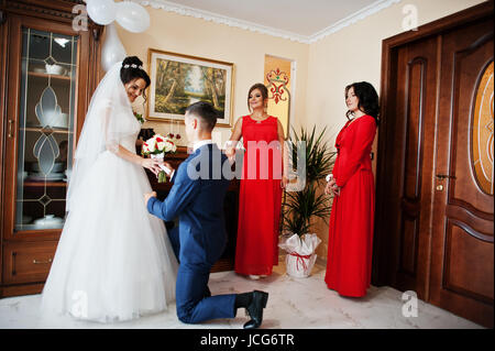 Bräutigam kniet küßt Hand einer Braut und gibt ihr einen schönen Strauß Rosen. Stockfoto