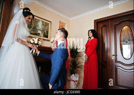 Bräutigam kniet küßt Hand einer Braut und gibt ihr einen schönen Strauß Rosen. Stockfoto