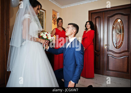 Bräutigam kniet küßt Hand einer Braut und gibt ihr einen schönen Strauß Rosen. Stockfoto