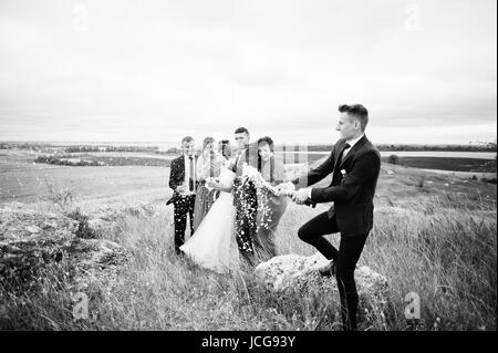 Brautführer oder Trauzeuge, die Öffnung der Flasche Champagner auf dem Lande mit Hochzeitspaar und Braidsmaids mit Brautführer stehend in die Hinterg Stockfoto