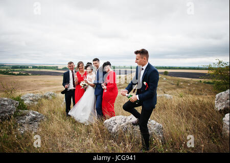 Brautführer oder Trauzeuge, die Öffnung der Flasche Champagner auf dem Lande mit Hochzeitspaar und Braidsmaids mit Brautführer stehend in die Hinterg Stockfoto