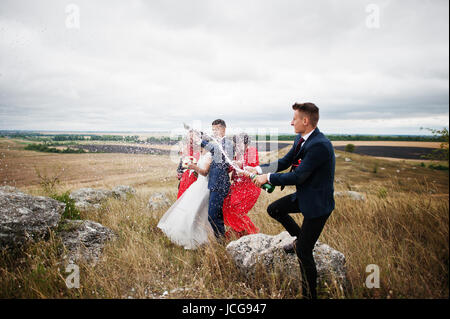 Brautführer oder Trauzeuge, die Öffnung der Flasche Champagner auf dem Lande mit Hochzeitspaar und Braidsmaids mit Brautführer stehend in die Hinterg Stockfoto