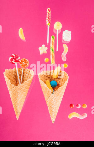 Waffelkegeln mit verschiedenen köstlichen Gelee Bonbons und Lutscher auf rosa Stockfoto