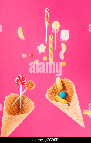Waffelkegeln mit verschiedenen köstlichen Gelee Bonbons und Lutscher auf rosa Stockfoto
