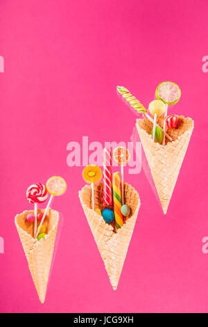 Waffelkegeln mit verschiedenen köstlichen Gelee Bonbons und Lutscher auf rosa Stockfoto