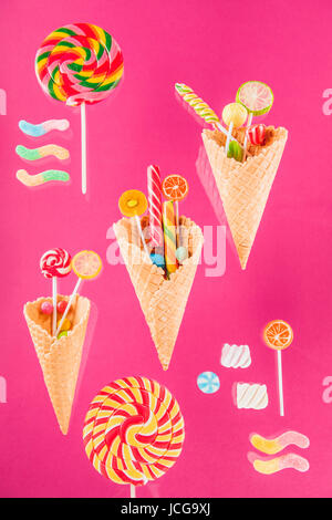 Waffelkegeln mit verschiedenen köstlichen Gelee Bonbons und Lutscher auf rosa Stockfoto