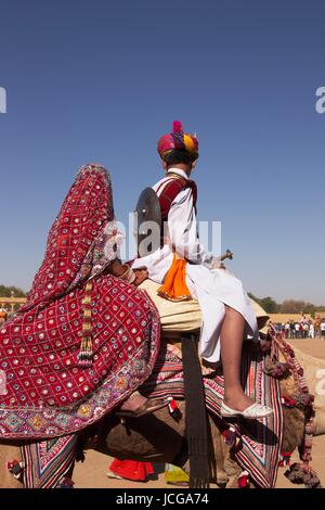 Indischen Jungen und Mädchen gekleidet in traditioneller Kleidung ein Kamel reiten, im Rahmen des jährlichen Wüste Festival in Jaisalmer, Rajasthan, Indien. Stockfoto