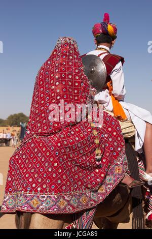 Indischen Jungen und Mädchen gekleidet in traditioneller Kleidung ein Kamel reiten, im Rahmen des jährlichen Wüste Festival in Jaisalmer, Rajasthan, Indien. Stockfoto