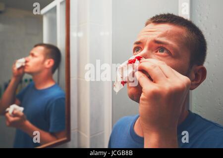 Mann mit Nasenbluten im Badezimmer. Für Themen wie Krankheit, Unfall oder Gewalt. Stockfoto