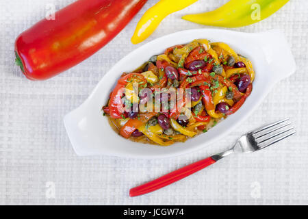 Paprika gekocht in Pfanne mit Öl, Oliven und Kapern. Typisch italienische Küche, zum Verzehr bereit. Weiße Schale auf weißem Hintergrund. Stockfoto