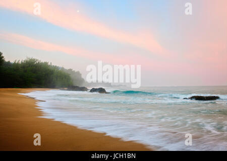 Mond setzt bei Sonnenaufgang entlang des nördlichen Ufers am Lumahai Beach auf Hawaii Insel Kauai. Stockfoto