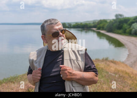 Outdoor Portrait von senior Mann tragen dunkle Sonnenbrille und Strohhut stehen auf "Dnipro" am Flussufer im Sommer Stockfoto