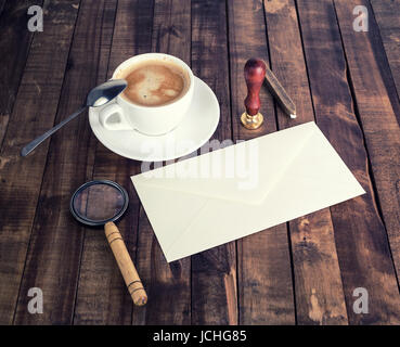 Foto von Vintage Briefpapier. Leere Hülle, Lupe, Siegel, Stempel, Kaffeetasse und Löffel auf hölzernen Hintergrund. Stockfoto