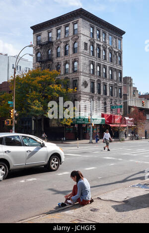 NEW YORK CITY - 16. Oktober 2014: Junges Mädchen sitzt auf dem Bürgersteig auf der 2nd Avenue mit ihren Füßen auf der Straße, vor einer typischen Solitär Ost gegen Stockfoto