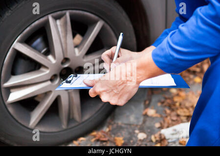 Nahaufnahme der Arbeitnehmer schriftlich in Zwischenablage sitzen in der Nähe von Auto Stockfoto