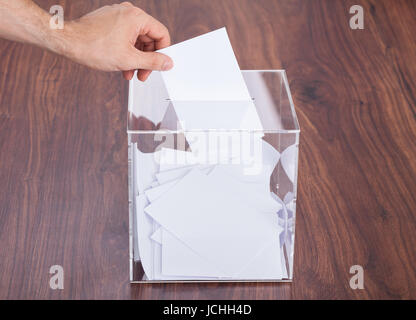 Nahaufnahme der Hand Person setzen Stimmzettel In Box gehalten auf Holztisch Stockfoto