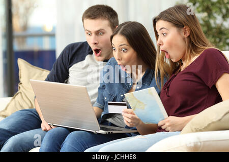 Drei Freunde zu finden, auf Linie mit einem Laptop sitzt auf einer Couch im Wohnzimmer in einem Haus Interieur bietet erstaunt Stockfoto