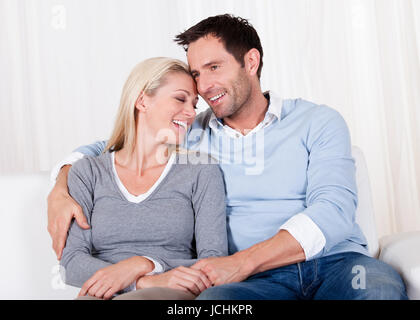 Romantischen jungen Paares zum Ausdruck ihrer Liebe durch die Nase zu reiben, da sie nah beieinander auf einem Sofa sitzen Stockfoto