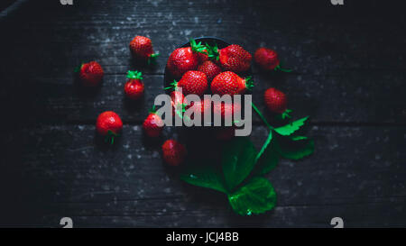 Erdbeeren in einer Schüssel mit Blättern auf einem alten Holzbrett Stockfoto