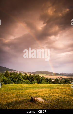 Regenbogen über dem Dorf auf dem Hügel und stürmischen Himmel Stockfoto