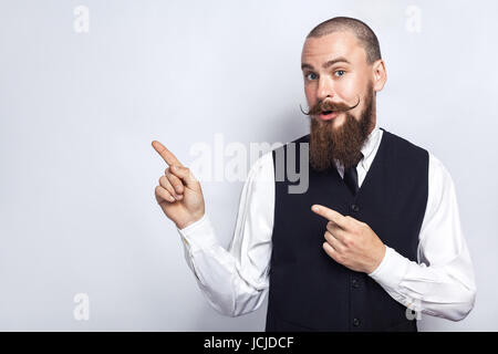 Gut aussehend Geschäftsmann mit Bart und Schnurrbart Blick auf Kamera, überrascht und zeigt textfreiraum mit Fingern. Studio gedreht, am grauen staatlich Stockfoto