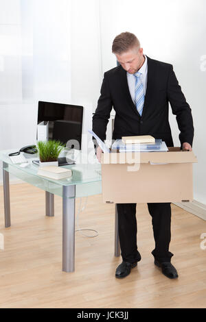 Niedergeschlagen Geschäftsmann gemacht redundante oder gebrannten tragen einen Karton voller seine persönlichen Sachen mit seinem niedrigen Kopf, als er sein Büro verlässt Stockfoto