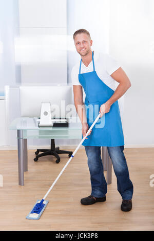 Gut aussehend männlichen Hausmeister oder Reiniger Reinigung des Bodens in einem Bürogebäude mit einem Mopp, waschen die und desinfizieren Sie die Oberfläche Stockfoto