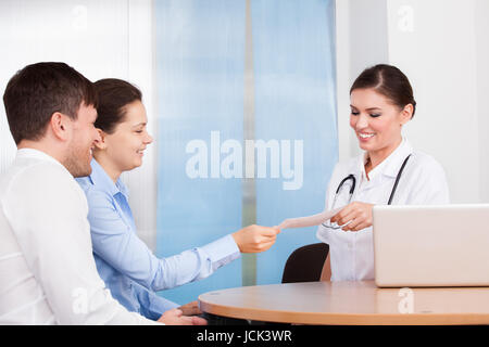 Glückliches junges Paar geben Umschlag zu weiblichen Arzt Klinik Stockfoto