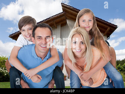 Mutter und Vater den Kindern A Huckepack vor Haus Stockfoto