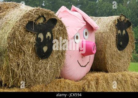 Comic-Tiergesichtern Vertretung Schafe und ein rosa Schwein schmücken drei Heuballen, angeordnet in einem Feld in der Nähe von Dorchester. Dorset, England, Vereinigtes Königreich. Stockfoto