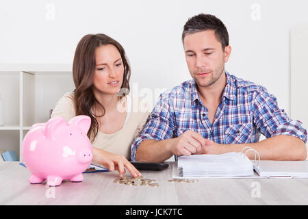 Junger Mann, Blick auf Frau einfügen Münze im Sparschwein Stockfoto