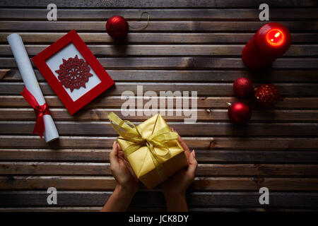 Goldene Geschenkverpackung in weiblichen Händen und Gegenständen Xmas auf hölzernen Hintergrund Stockfoto