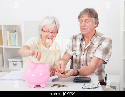 Portrait Of Smiling älteres paar Münzen In die rosa Sparschwein Berechnung Stockfoto