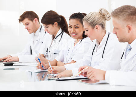 Ärzteteam schreiben am Schreibtisch sitzend in einer Reihe Stockfoto
