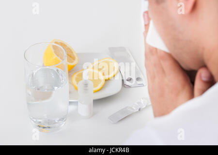 Zugeschnittenes Bild der Mann leidet unter Kälte mit Medikamenten und Wasserglas auf Tisch Stockfoto