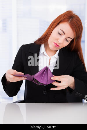 Aufgeregt junge Geschäftsfrau Blick auf leere Brieftasche beim Sitzen am Schreibtisch Stockfoto