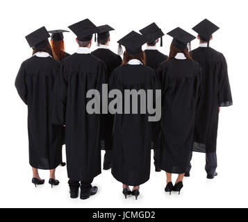 Große Gruppe von Absolventen stehen in den Kleidern und Quaste Hüte angesehen von hinten isoliert auf weiss Stockfoto