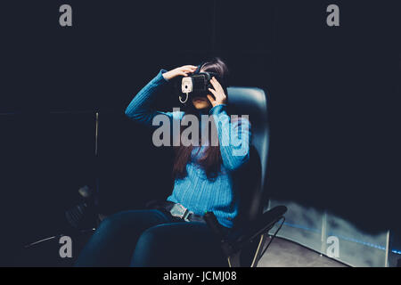 Junge schöne östlichen Frau sitzen auf einer Gaming-Stuhl testen erweiterten Realität mit 3D Viewer - Spiele, futuristisch, augmented Reality-Konzept Stockfoto