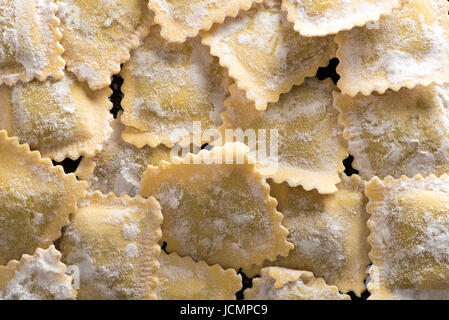 Von oben Blick auf rohe handgefertigte italienische Ravioli Pasta mit Mehl auf schwarzem Hintergrund bedeckt. Essen-Textur Stockfoto