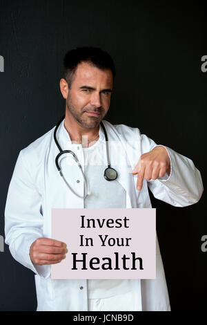 hübscher Arzt mit einem Schild mit den Worten investieren In Ihre Gesundheit Stockfoto