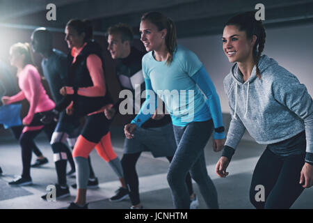 Gruppe junger Sportler trainieren in einer städtischen Parkhaus Schlange bereit zu einer Rasse oder Praxis laufen ihre sprinten mit glücklichen Lächeln in einem Gesundheit Stockfoto