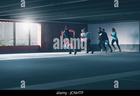 Gruppe von entschlossenen jungen Athleten urban laufen, sprinten durch einen kommerziellen Parkhaus in einem Training Training, Sonne Flare Streiflicht und Kopie Stockfoto