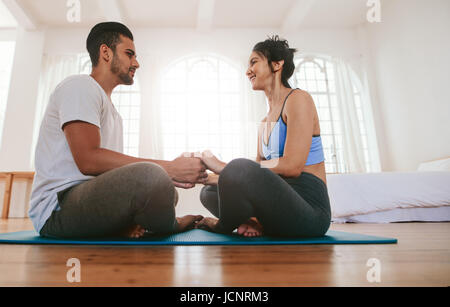 Seitenansicht der junge Mann und Frau zu Hause Yoga zu tun. Paar-Sitzung auf der Yoga-Matte, Hand in Hand zusammen. Stockfoto