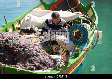 Ein Fischer flickt seine Netze in seinem Luzzu Fischerboot im Hafen von St Julians Bay Malta an einem sonnigen Sommertag Stockfoto